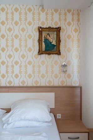 Una habitación de hotel con una cama, una mesita de noche, un cuadro en la pared y un interruptor de luz.