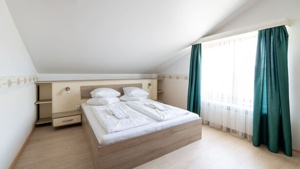 Een slaapkamer met een bed, een houten hoofdbord, een nachtkastje, een dressoir en een raam met gordijnen.