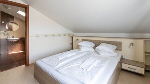 Een slaapkamer met een bed, nachtkastje, spiegel en een badkamer met een wastafel.