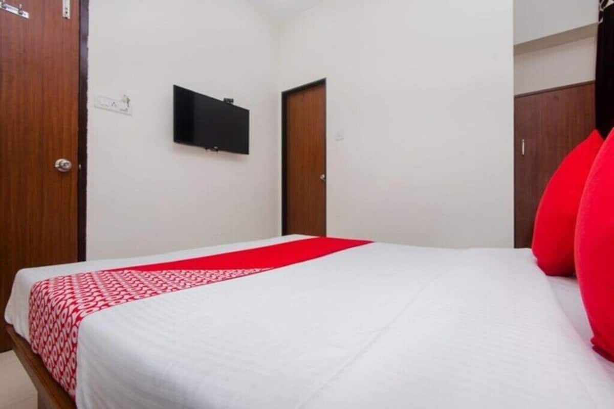 Hotellihuone, jossa on sänky, seinälle asennettu televisio ja ovi.