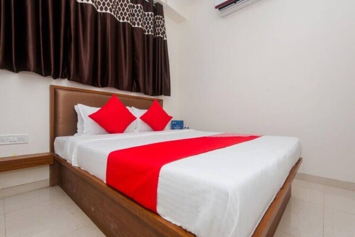 A neatly made bed with a wooden headboard, white bedding, and red accents.