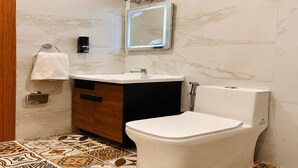 Een badkamer met een marmeren wand, een wit toilet, een wastafel met spiegel en een handdoekhouder.