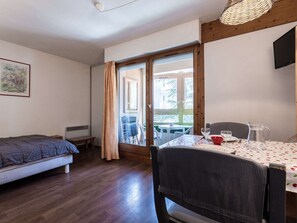 Ein Zimmer mit einem Bett, einem Esstisch mit Stühlen, einem Fenster mit Vorhängen und einem Fernseher.