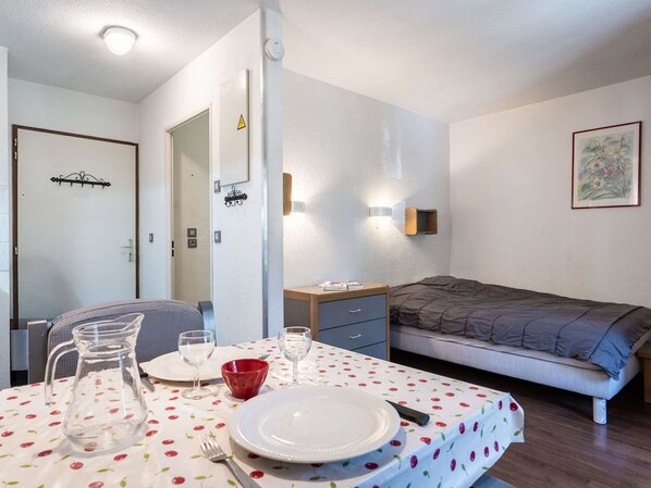 Een kleine, goed verlichte kamer met een bed, een nachtkastje en een tafel gedekt voor twee personen, met borden, glazen en een karaf.