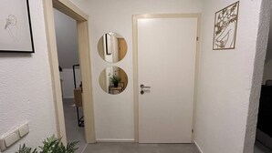Un couloir avec une porte blanche, deux miroirs ronds, une petite étagère avec une plante et un tableau encadré accroché au mur.