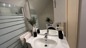 Une salle de bain avec un lavabo blanc, un miroir, un porte-serviettes et une plante en pot.