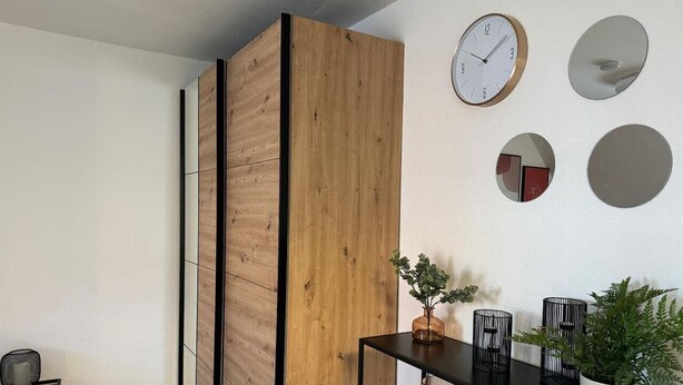 Une pièce moderne avec une cloison en bois, une table à manger avec des chaises, une horloge et un miroir au mur.