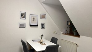 Un coin repas avec une table blanche, quatre chaises grises et des tableaux encadrés accrochés au mur.