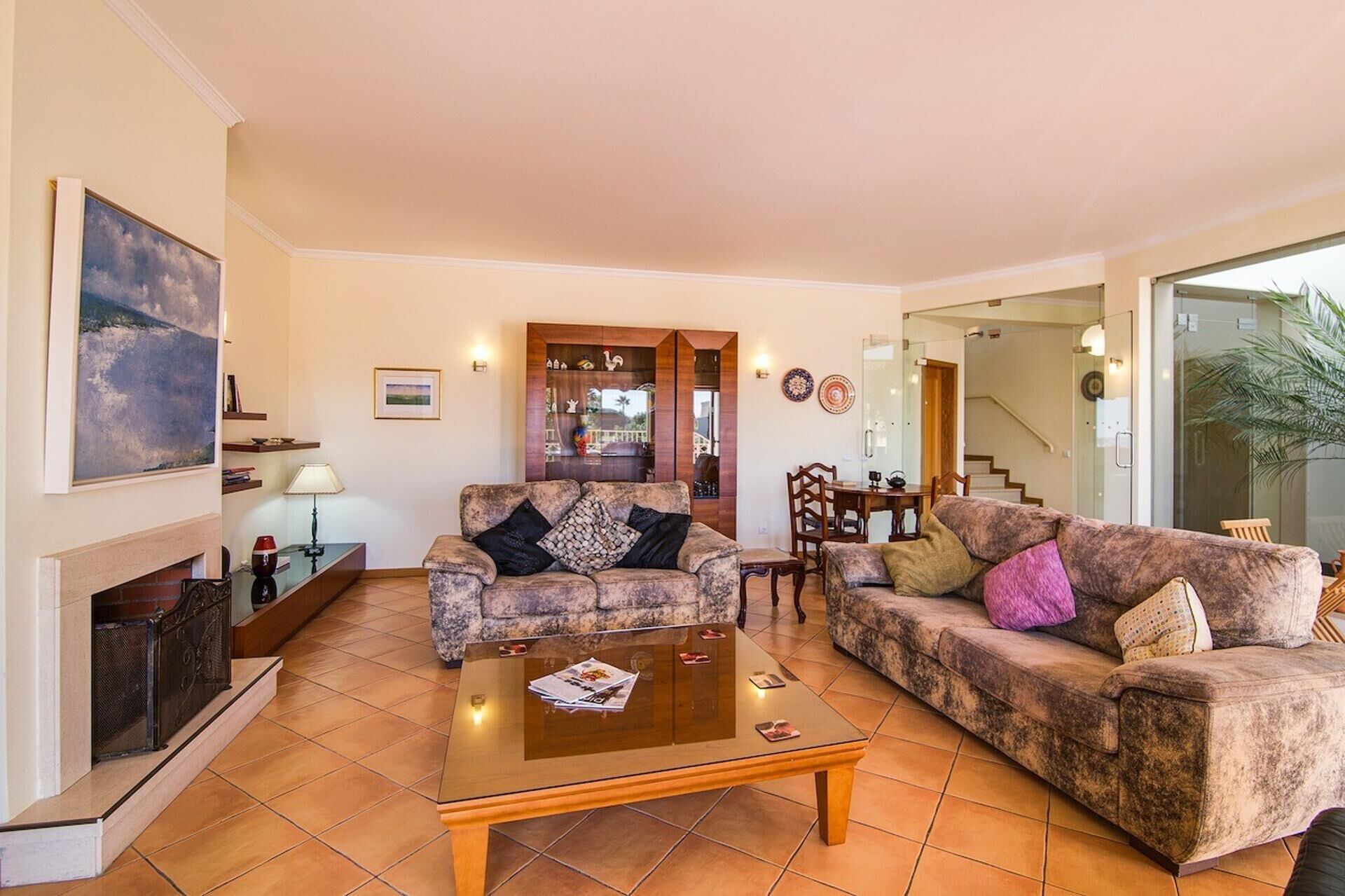 A living room with two sofas, a coffee table, a fireplace, and a dining area visible through an open door.