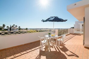 Eine Terrasse mit Tisch, Stühlen und Sonnenschirm mit Blick auf eine Stadtlandschaft.