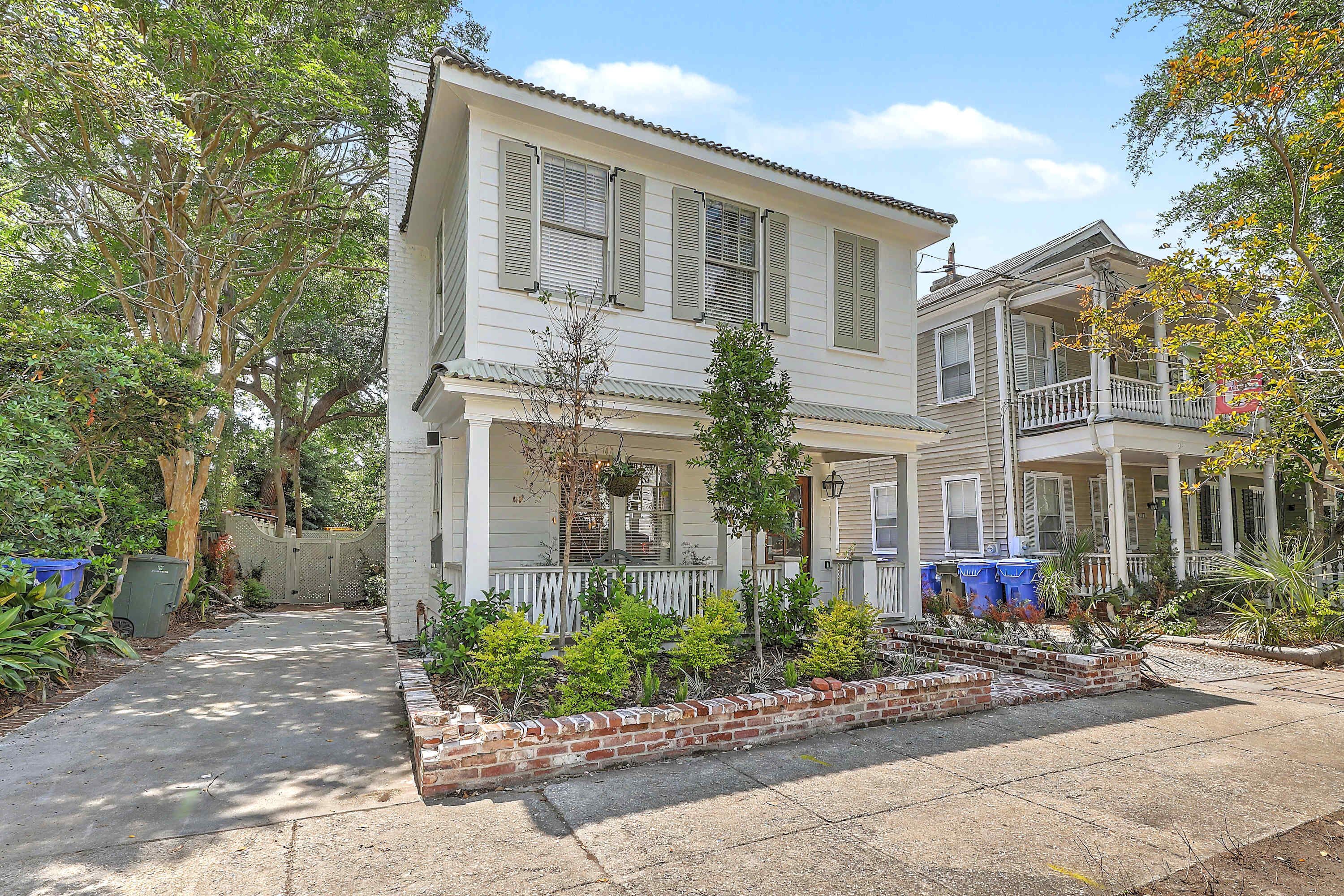 A two-story house with a front porch, a brick garden bed, and a fence.