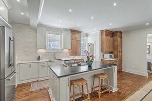 Eine moderne Küche mit weißen Schränken, einer zentralen Kochinsel, Holzstühlen und einem Edelstahl-Kühlschrank.