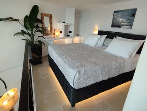 A modern bedroom with a large bed, bedside tables, a mirror, a potted plant, and a painting on the wall.
