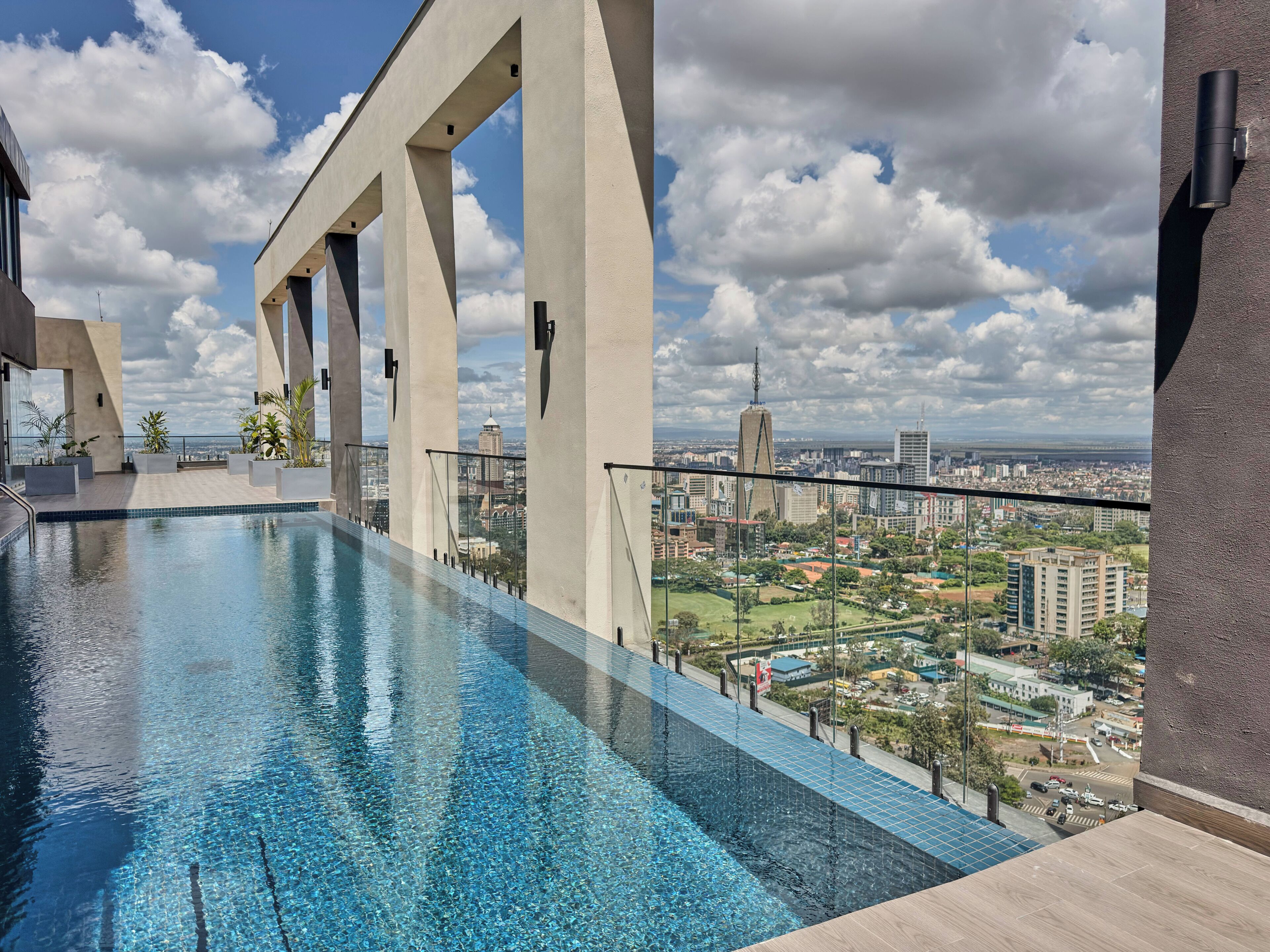 A rooftop infinity pool with a city view, supported by large pillars, and a clear sky.