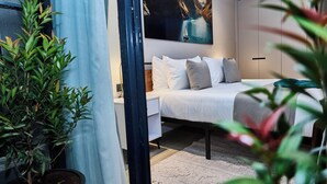 A bedroom with a bed, a nightstand, a potted plant, and a painting on the wall. - Novelle By Edmor Suites (Nairobi)