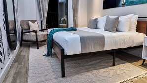 A bedroom with a bed, a chair, a large window, and a painting on the wall. - Novelle By Edmor Suites (Nairobi)