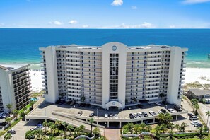 Ein mehrstöckiges Hotel mit zentralem Eingang, Parkplatz und Blick auf Strand und Meer.