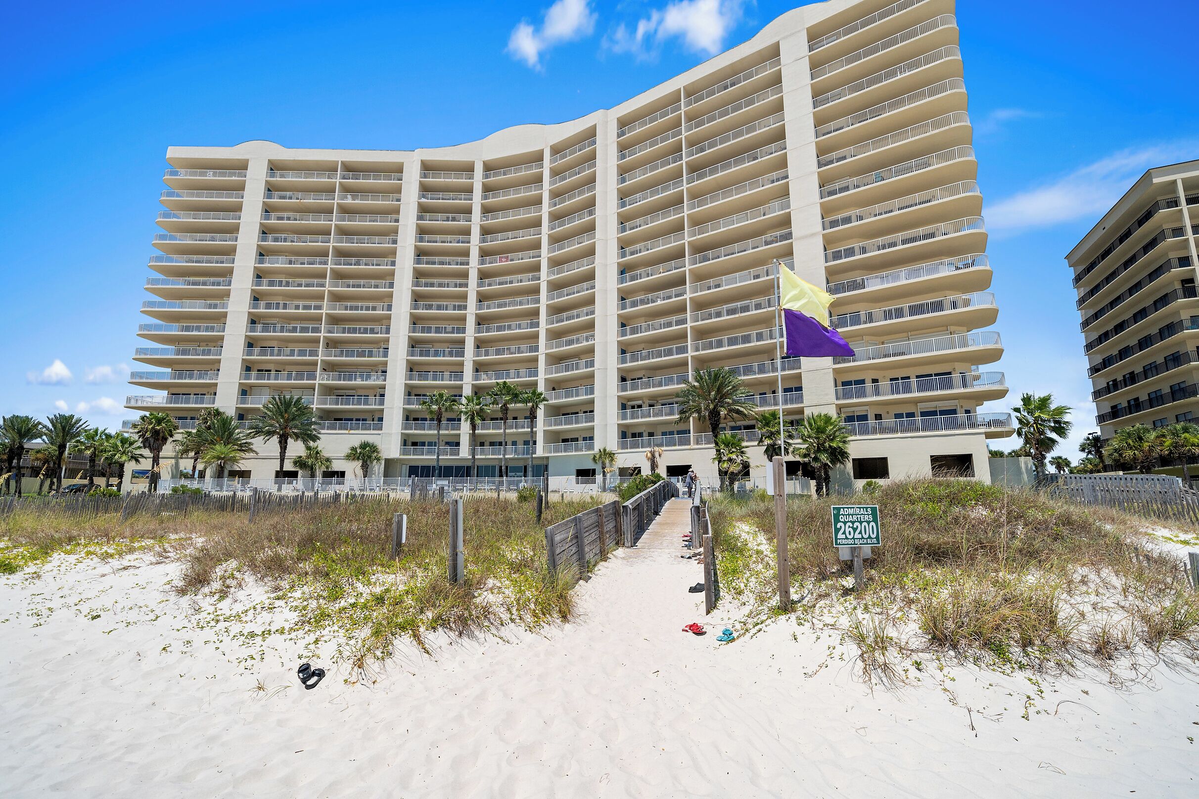 A large hotel with multiple balconies, a sandy beach in front, and a sign indicating room rates.