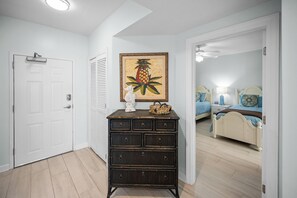 Ein Zimmer mit einer weißen Tür, einem dunklen Holzschrank, einer Kunstdruck-Ananas in einem Rahmen und einem Bett mit blauer Bettwäsche.
