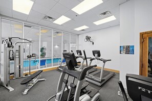 Ein Fitnessraum mit Trainingsgeräten, ein Fenster mit Blick auf einen Pool und ein Schild, das Personen unter 16 Jahren den Zutritt untersagt.