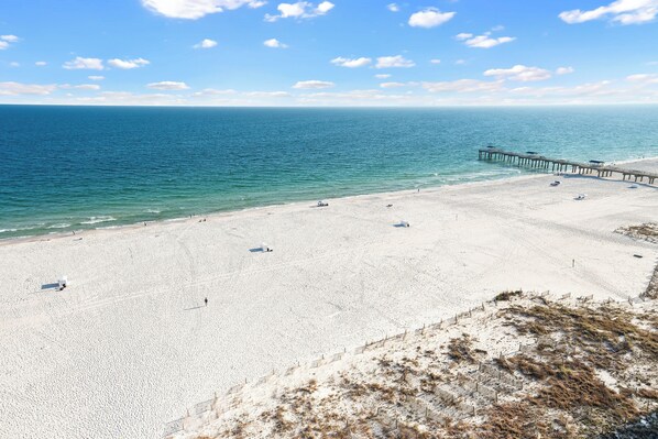 Ein Strand mit einem Steg, der ins Meer hinausführt, feinem Sand und blauem Himmel.