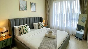 Ein Hotelzimmer mit einem großen Bett, zwei an der Wand befestigten Kunstwerken, einem Nachttisch mit Lampe und Blick auf die Stadt durch transparente Vorhänge.
