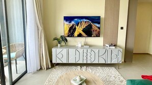 Ein modernes Wohnzimmer mit einem großen Gemälde, einem weißen Schrank, einer Pflanze und Blick durch eine Glastür.