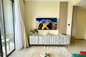 Ein modernes Wohnzimmer mit einem großen Gemälde, einem weißen Schrank, einer Pflanze und Blick durch eine Glastür.