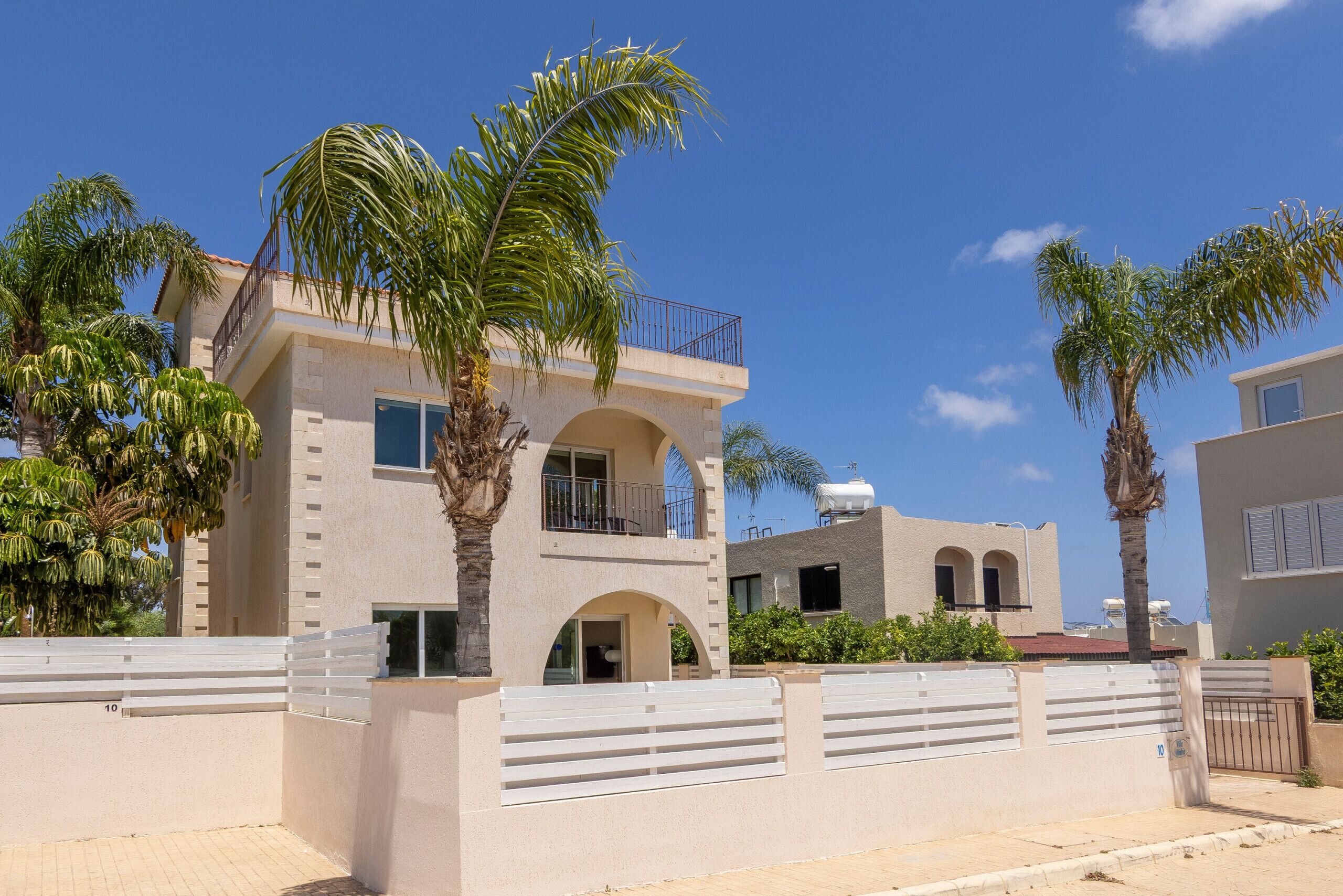 A two-story building with a balcony, palm trees, and a gated entrance.