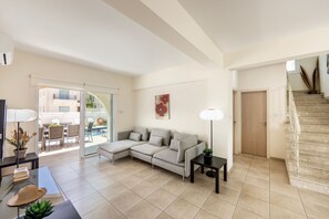 Ein Wohnzimmer mit Ecksofa, Glastür zum Balkon, Treppe und Flachbildfernseher.
