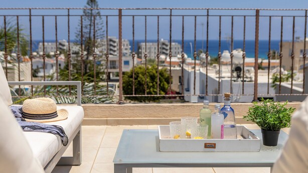 A balcony with a white sofa, a hat, a tray with drinks, and a potted plant. - Protaras Seaside Villa Andria (Paralimni)