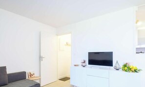 A modern living room with a grey sofa, a flat-screen TV on a white cabinet, and a door leading to another room. - Cozy apartment - 4 guests, heart of Biscarrosse Beach (Biscarrosse)