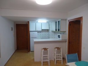 Eine kleine Küche mit weißen Schränken, einem Kühlschrank, einer Mikrowelle und zwei Barhocker.
