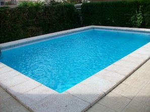 Ein rechteckiger Pool mit einer gefliesten Kante und einem von einem Kieselmuster geprägten Deck drumherum.