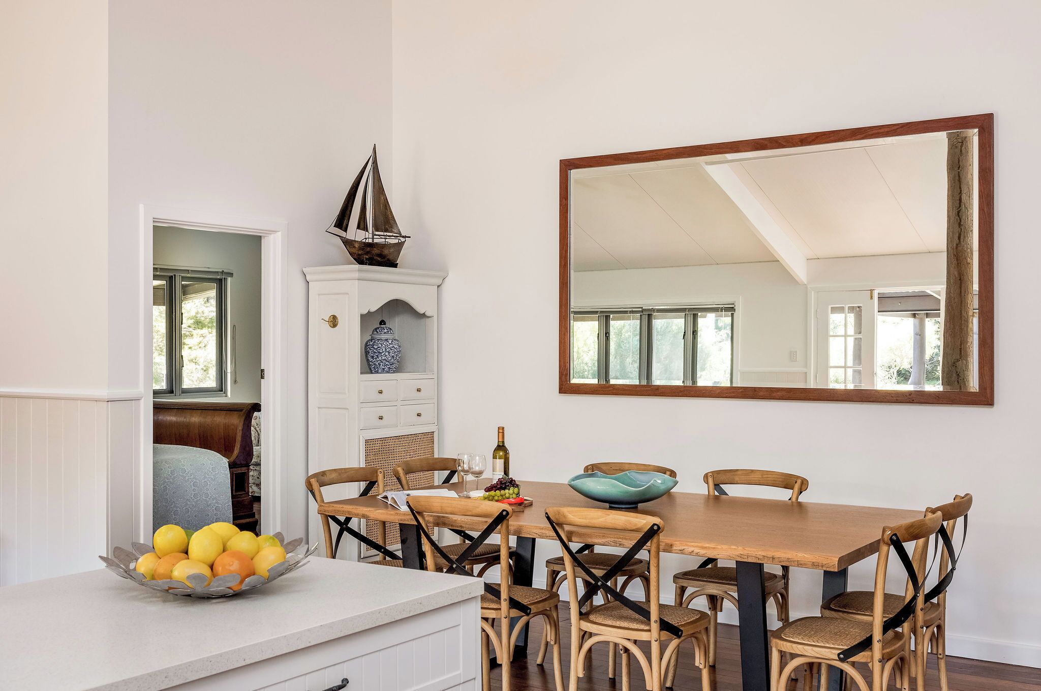 A dining area with a wooden table, wicker chairs, a large mirror, and a cabinet with decorative items.