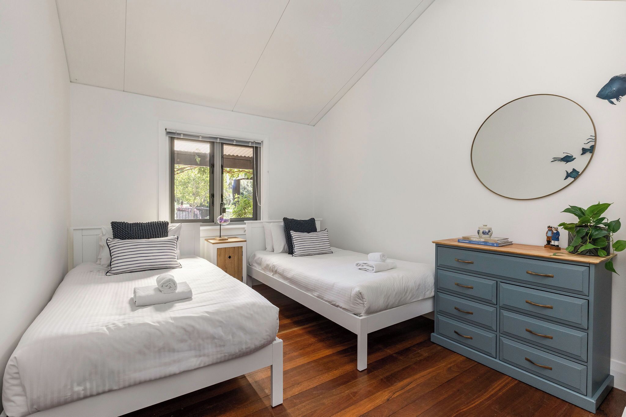 A bedroom with two beds, a dresser, a mirror, and a window.