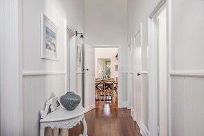 A hallway with white walls, a wooden floor, a white console table with a vase, and a dining area in the background. - PEACEFUL AND SERENE RURAL COTTAGE SITUATED IN QUINDALUP ON 4.5 ACRES (Quindalup)