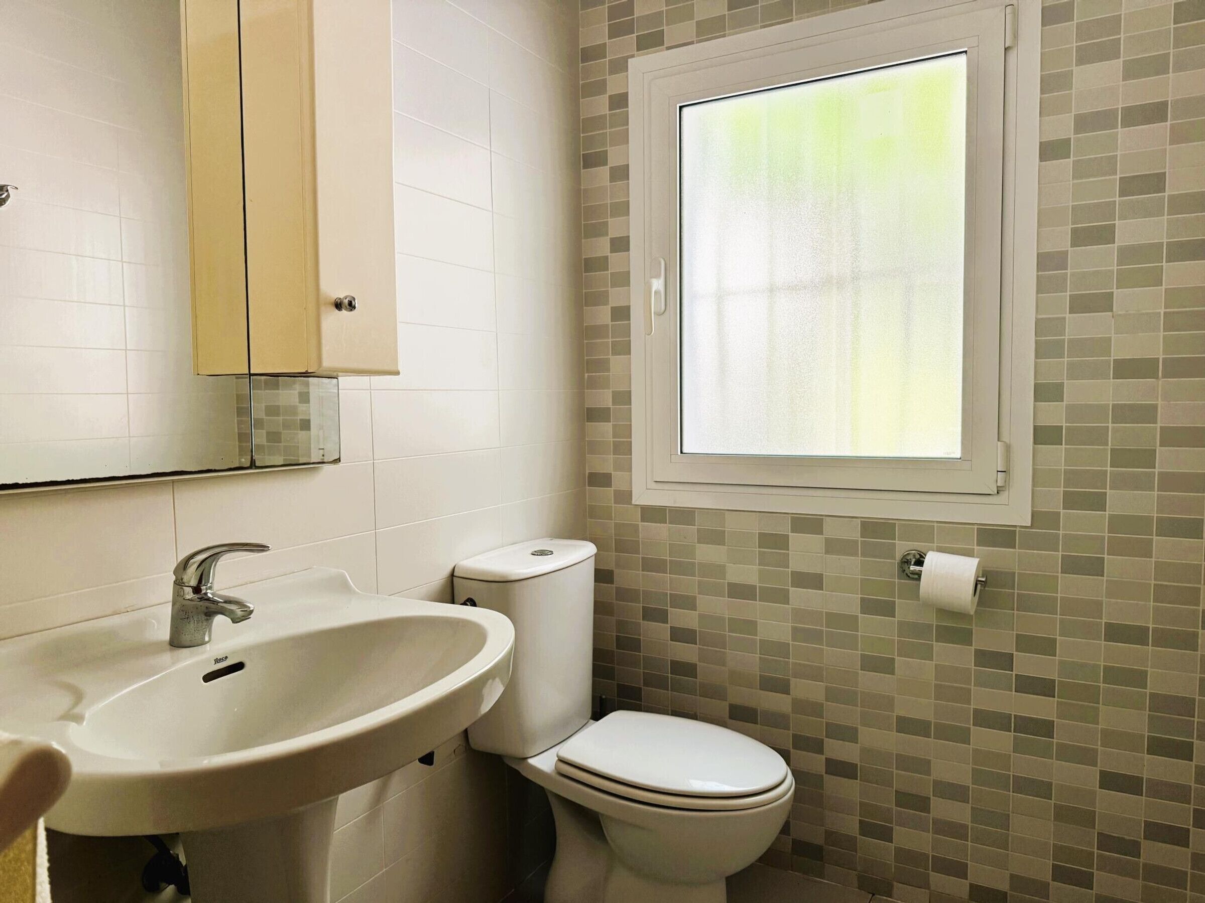 Une salle de bain avec un lavabo, des toilettes et une fenêtre.