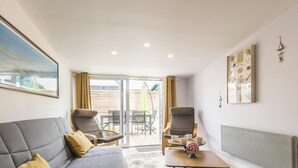 A modern living room with a grey sofa, a coffee table, and a dining area with chairs and a table. - House near beach, AC, parking - 2 guests (Gouville-sur-Mer)