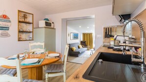 A compact kitchen with a sink, a microwave, and a dining area with a table and chairs. - House near beach, AC, parking - 2 guests (Gouville-sur-Mer)
