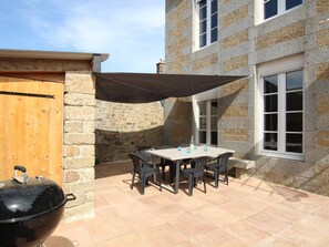 Eine Terrasse mit Tisch und Stühlen, einem Grill und einem Steinhaus mit Fenstern.