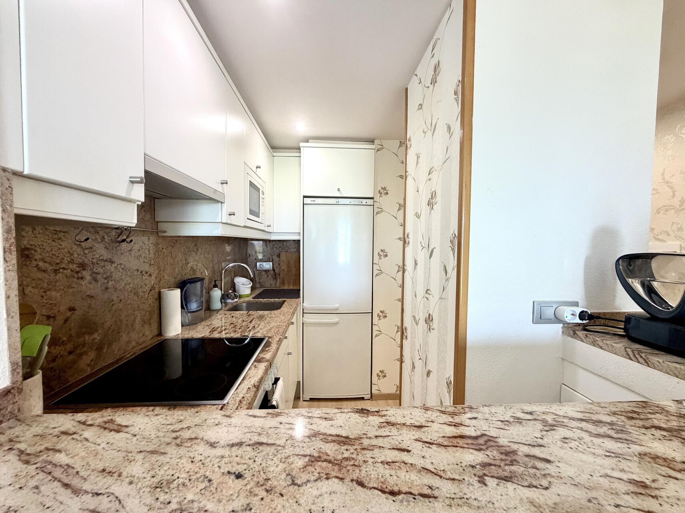 A compact kitchen with white cabinets, a built-in stove, a refrigerator, and a sink.
