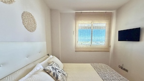 A bedroom with a bed, a window with blinds, a television on the wall, and a patterned rug. - Tranquil apartment, pets welcome - 4 guests (Roses)