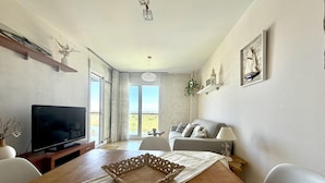A living room with a TV, sofa, dining table, and a view through the sliding doors. - Tranquil apartment, pets welcome - 4 guests (Roses)