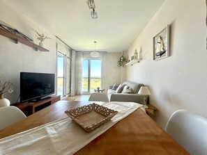 Ein Wohnzimmer mit Fernseher, Sofa, Esstisch und Blick durch Glastüren.