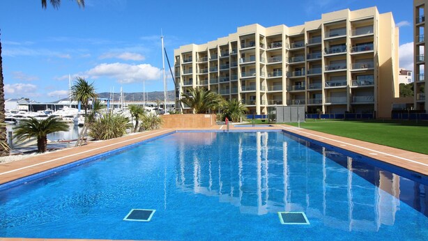 A swimming pool with a tiled deck, a marina with boats, and a multi-story building with balconies. - Tranquil apartment, pets welcome - 4 guests (Roses)