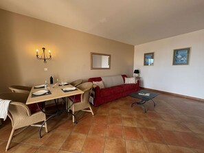 Ein Wohnzimmer mit Esstisch, Stühlen, einem roten Sofa, einem Couchtisch und einem Kronleuchter.
