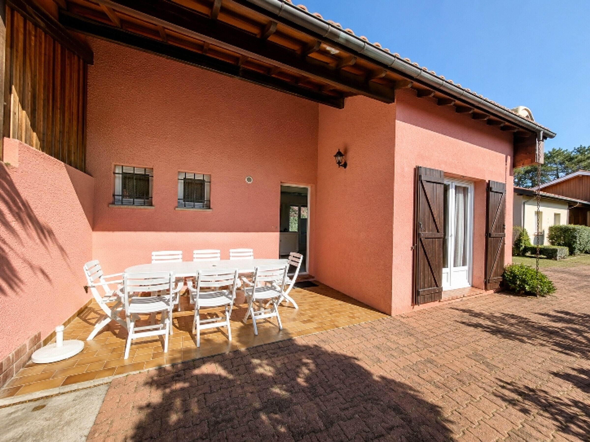 A building with a pink exterior, a covered patio with a table and chairs, and a door with a shutter.