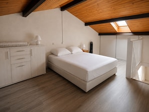 Ein Schlafzimmer mit Bett, Nachttisch, Lampe, Kommode und einem Oberlicht.
