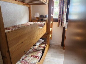 A bunk bed room with a wooden headboard, a bedside table with a lamp, and a window with curtains. - Cozy triplex apartment - 4 guests (32m²) (Avoriaz)